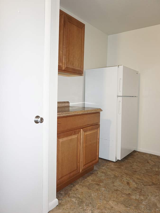 Galley kitchen with brown cabinets and white appliances at Patricia Court apartments in Lansdowne, PA.