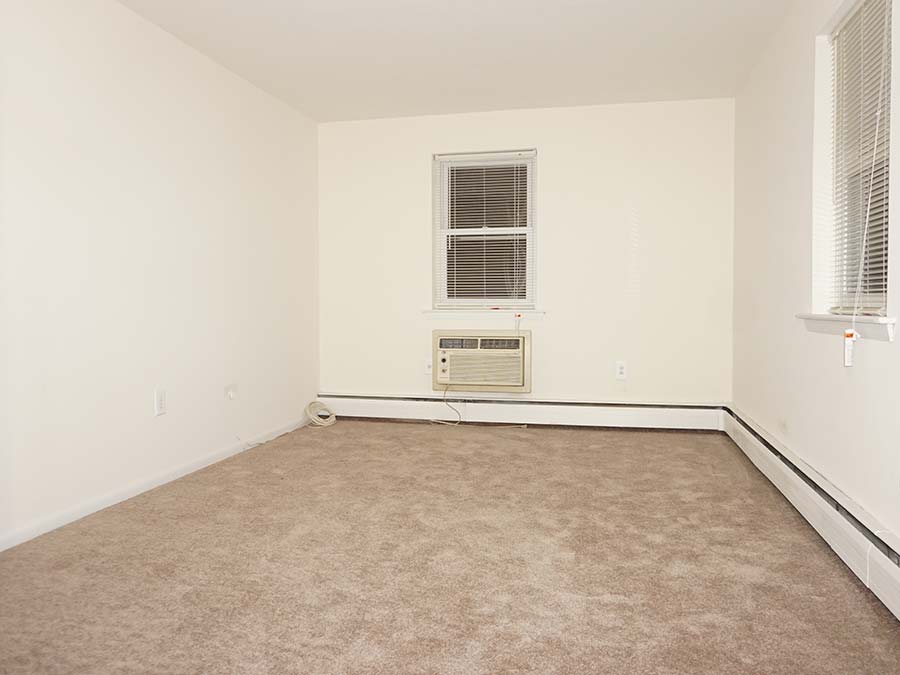 Carpeted bedroom with two windows and AC in Patricia Court apartments in Lansdowne, PA.