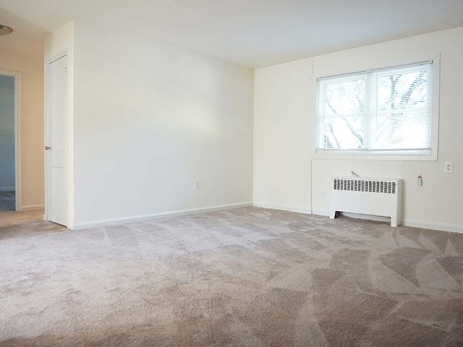 Carpeted living room with heating and a window in the Penzel Manor apartments in Upper Darby, PA.