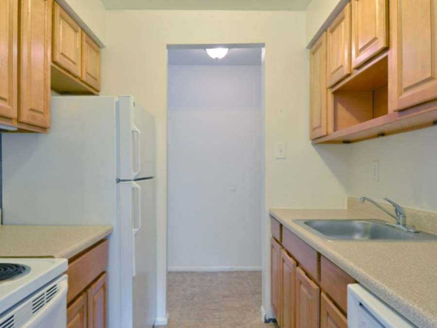 Galley kitchen with light brown cabinetry and white appliances in Ridgeway Court apartments in Lansdowne, PA.