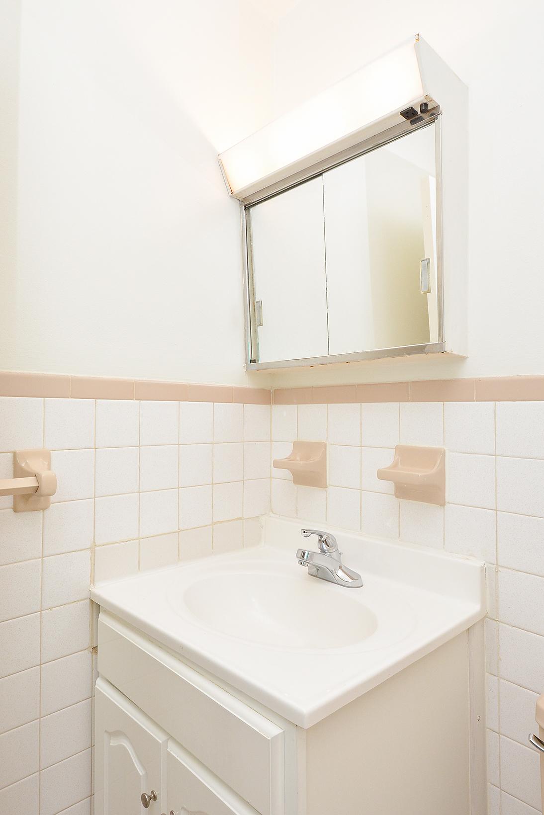 White sink and mirror with built-in soap dish in a bathroom at Hazel Apartments in Clifton Heights, PA.